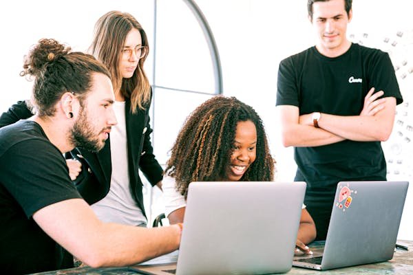 Trois apprenants sont autour de leur amie et l'observe en train de travailler sur son ordinateur portable.